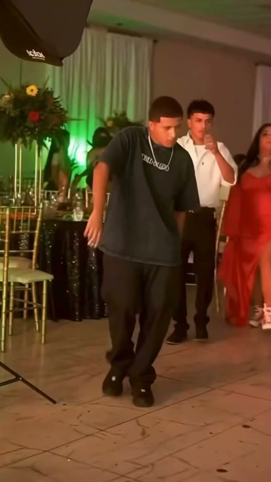 Dime Dime Baby trend clip: a young man in a dark T-shirt and silver chain dances toward the camera at a quinceañera